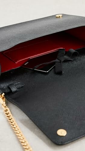 Open black leather handbag with red interior and gold chain.