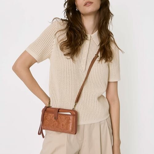 Woman wearing a beige knit top, holding a brown leather bag.